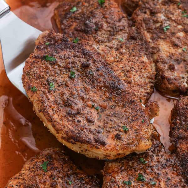Cooked pork chops in a baking dish with a serving on a spatula.