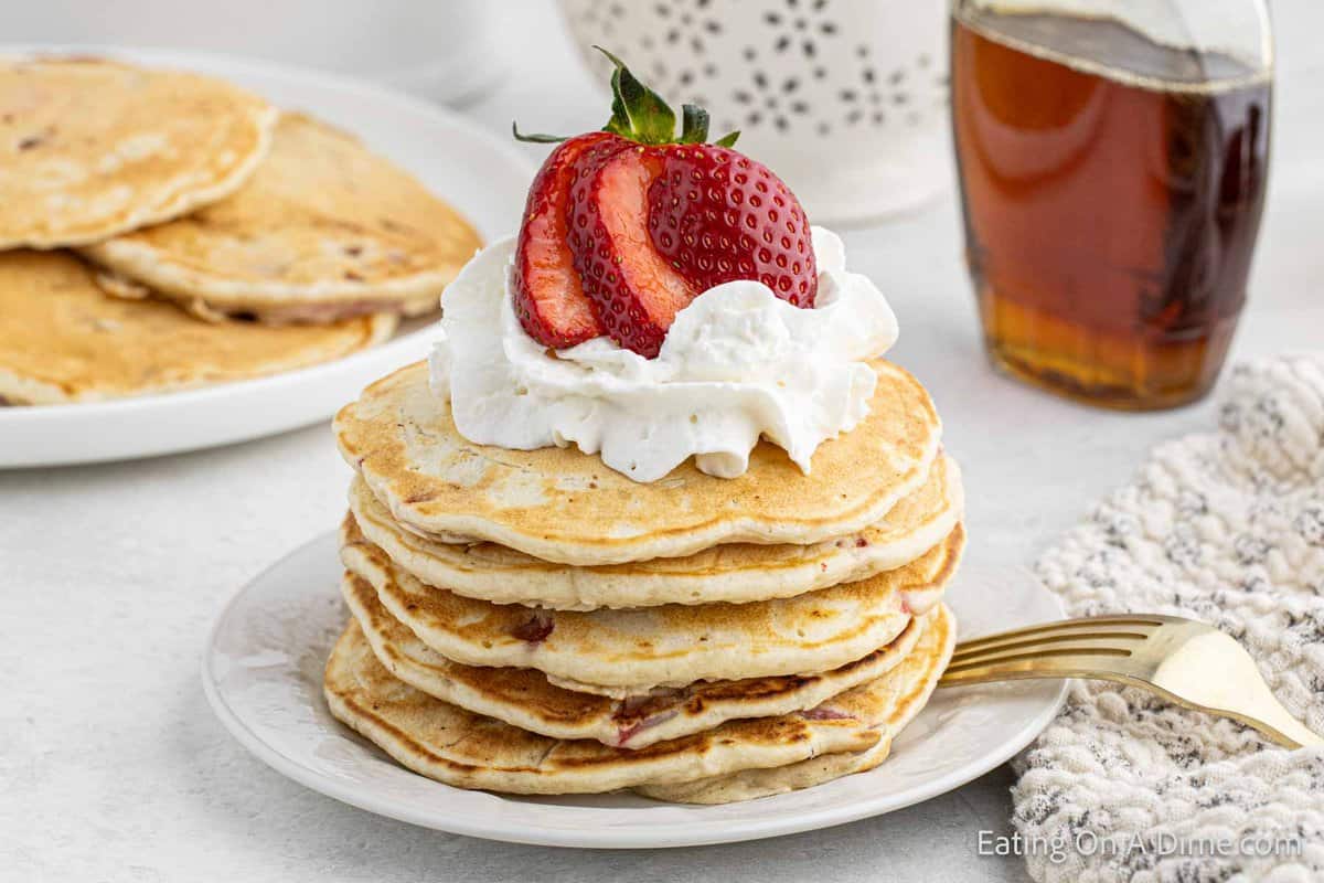 Stacked strawberry pancakes on a plate topped with whipped cream and strawberries
