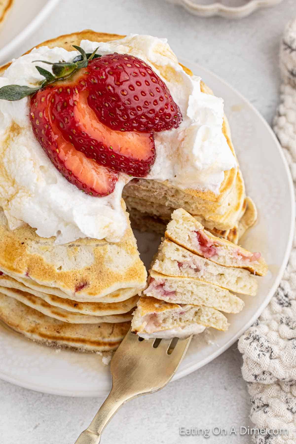 Pancakes Stacked on a plate topped with whipped cream and slice strawberries