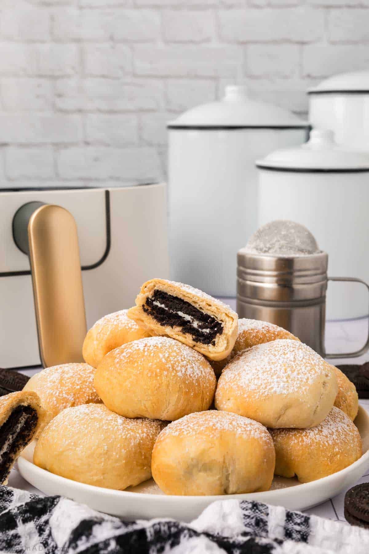 Air Fried Oreos with a golden brown crust stacked on a plate with a air fryer in the background