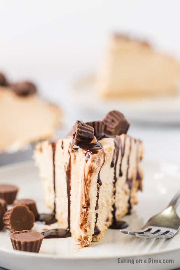 Close up image of a slice of peanut butter pie topped with mini peanut butter cups on a plate with a fork. 