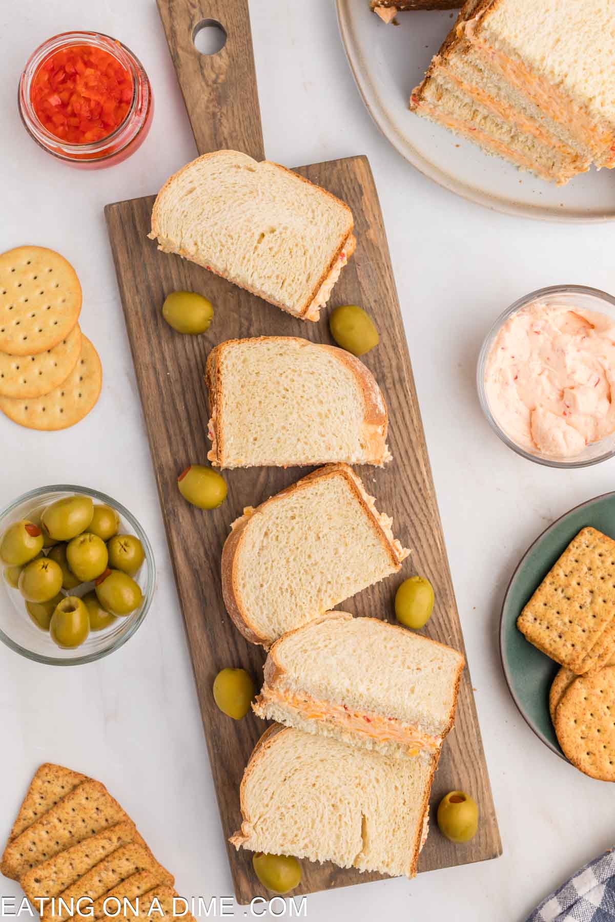 Pimento Cheese cut in half on a cutting board with bowls of green olives, crackers and pimento cheese