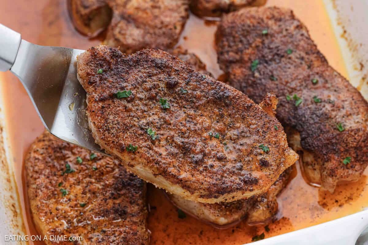 Oven Baked Pork Chops in a baking dish with one pork chop on a silver spatula. 
