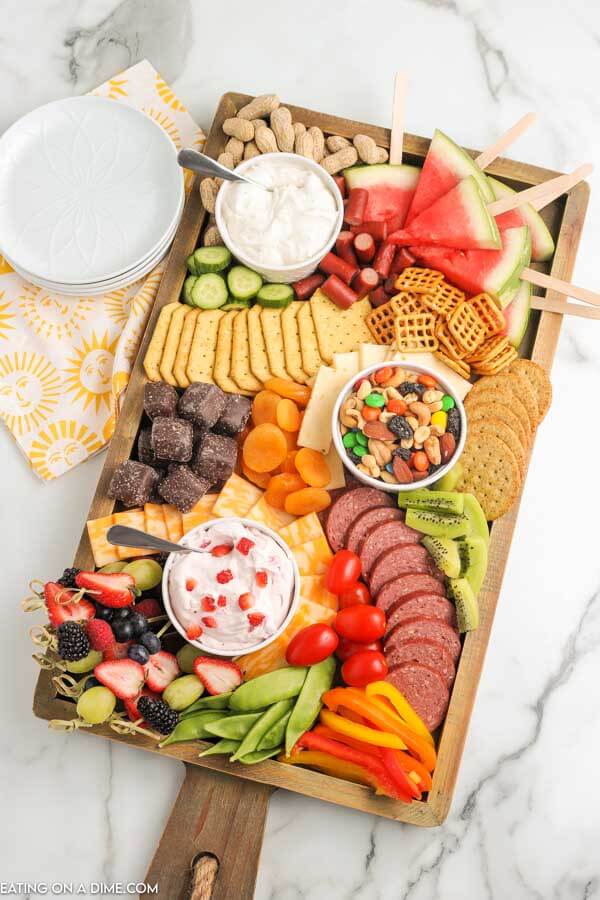 Summer charcuterie board with fruit, vegetables, chocolate, nuts and mote.