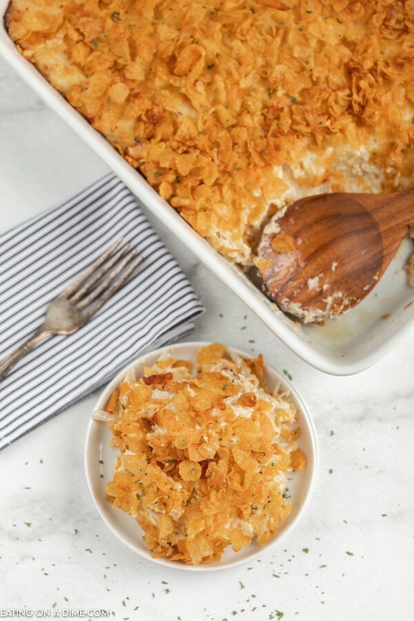 Close up image of a small serving of cheesy chicken casserole. Also a casserole dish with the cheesy chicken hashbrown casserole with a brown spoon.
