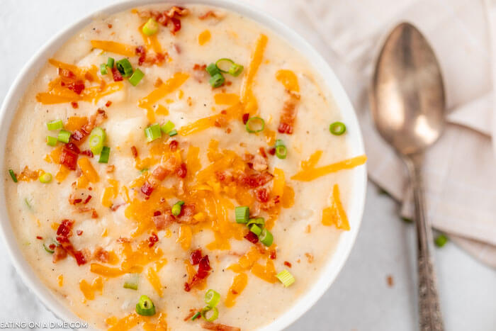 Close up image of potato soup topped with cheese, bacon bites and green onions