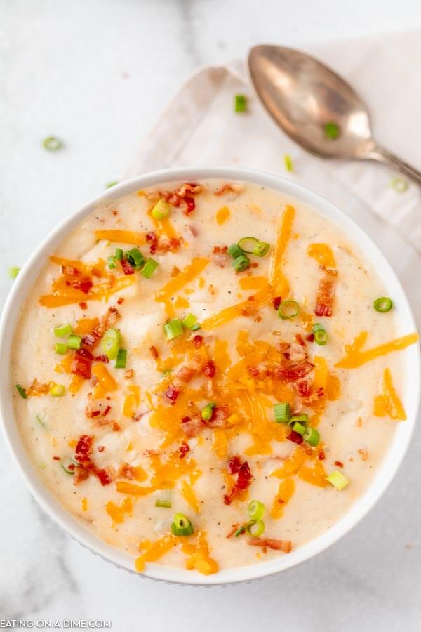 Close up image of potato soup topped with cheese, bacon bites and green onions
