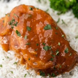 A pork chop over white rice topped with fresh parsley.