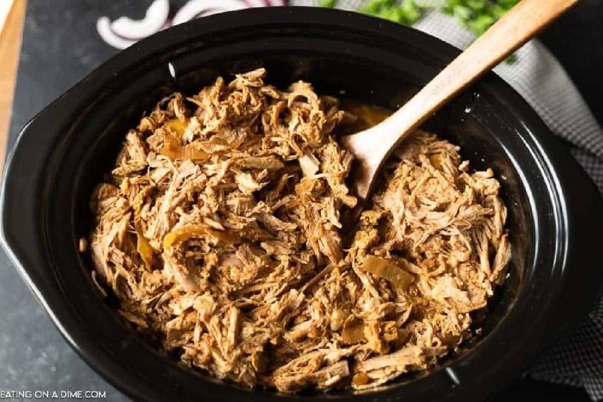 Shredded Pork in the slow cooker with a wooden spoon