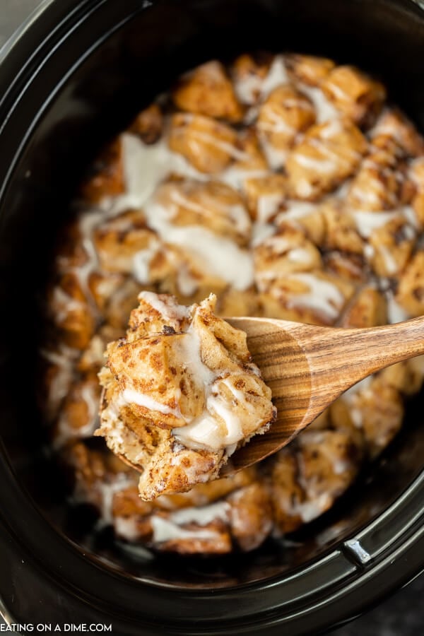 Close up image of crock pot cinnamon roll with a serving on a wooden spoon. 