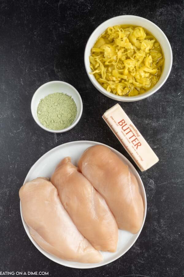 Close up image of ingredients for Mississippi chicken. It includes Peperoncini, ranch seasoning, butter, and chicken breast. 