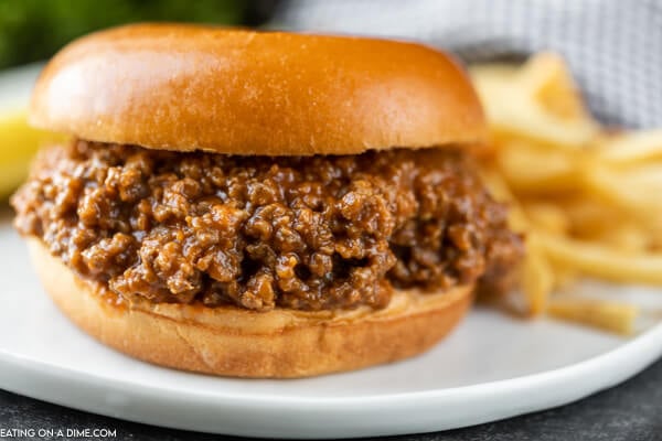 Close up image of sloppy joes on a bun. It is plated on a white plate with french fries. 