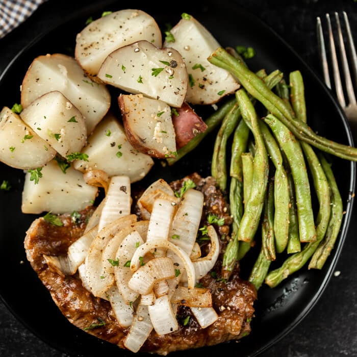 crockpot steak and onion served with diced potatoes and green beans on a plate.