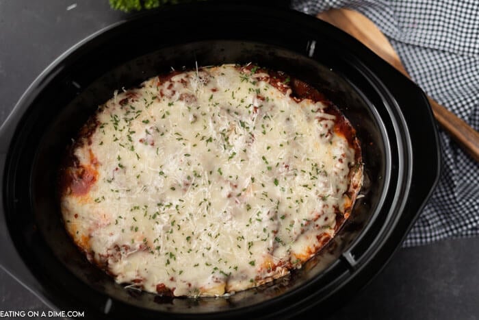Overview of this slow cooker lazy day lasagna recipe in a black crock pot with a large wooden spoon next to it. 