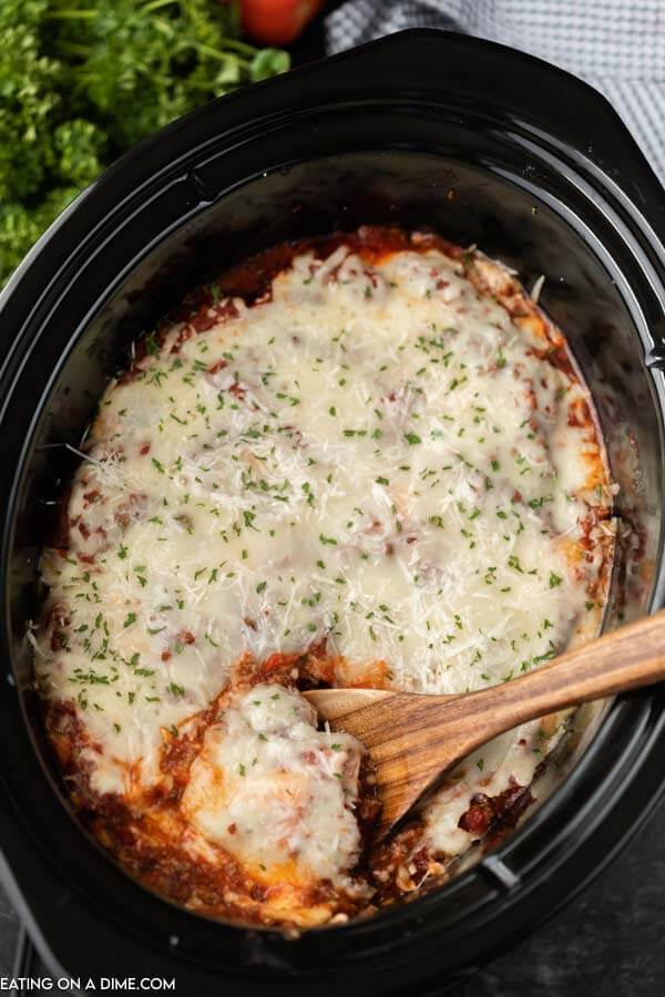 Overview of the Lazy Day Crock Pot Lasagna Recipe in the crock pot with a large spoon scooping out a serving. 