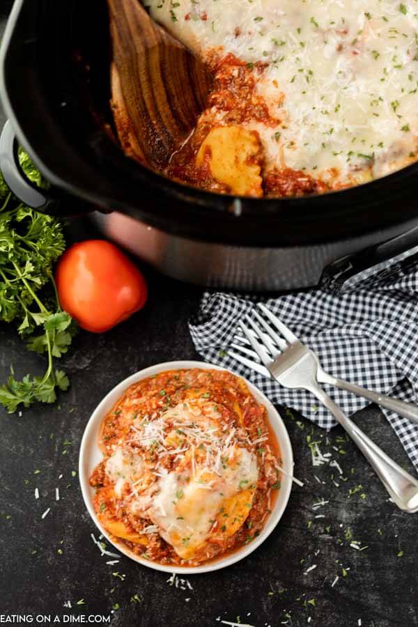 A plate of this lazy day crock pot lasagna recipe next to the crock pot with the rest of the lasagna in the crock pot.  