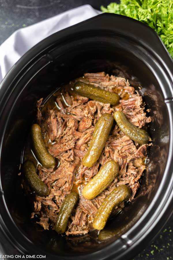 Dill pickle roast shredded in crock pot with pickles on top. 
