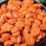 A plate of brown sugar glazed carrots, sliced and garnished with chopped herbs, arranged in a close-up view. The carrots appear glossy and vibrant orange.
