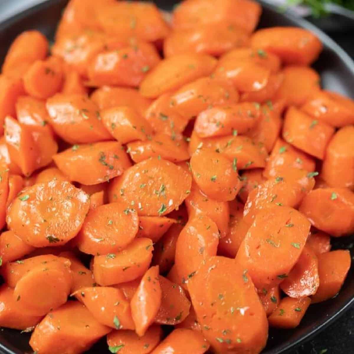 A plate of brown sugar glazed carrots, sliced and garnished with chopped herbs, arranged in a close-up view. The carrots appear glossy and vibrant orange.