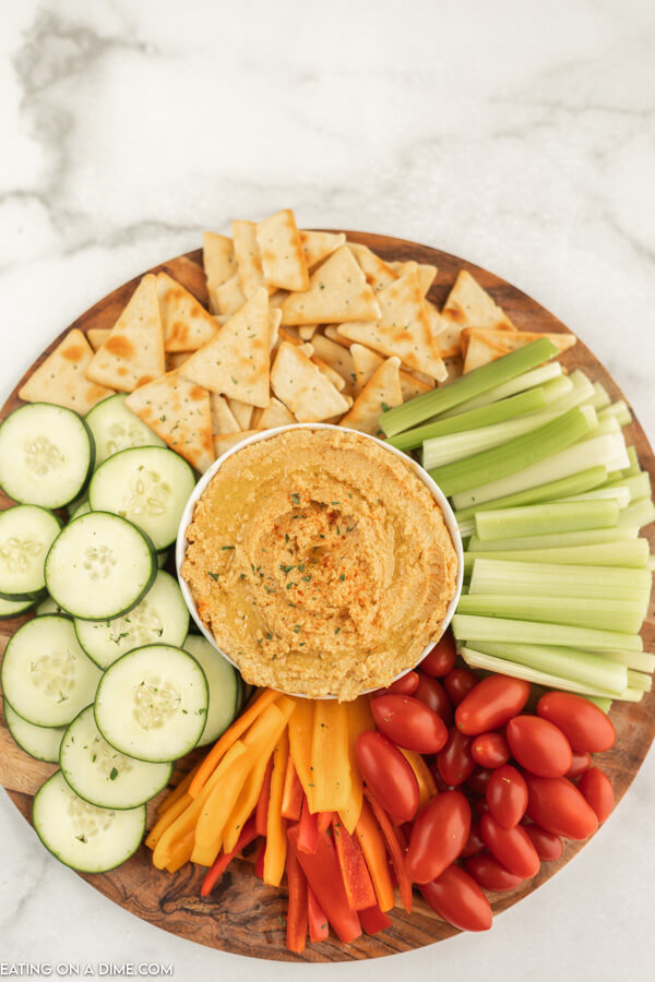 Platter of vegetables and pita chips with hummus in the middle.