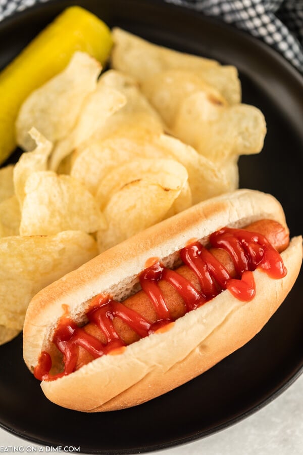 Plate with hot dog in a bun beside chips. 