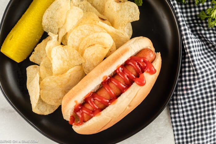 Plate with hot dog in a bun beside chips. 