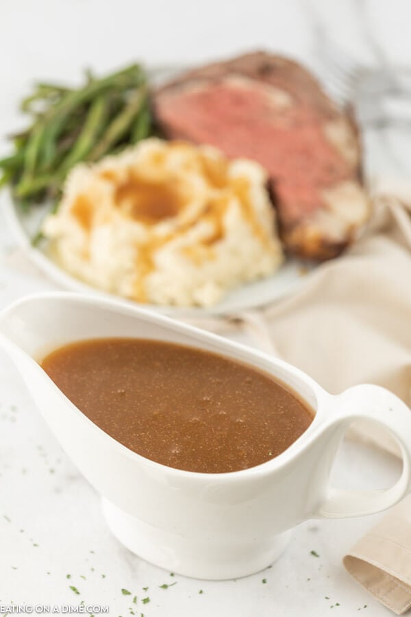 container of gravy in front of a plate with green beans, mashed potatoes with gravy and roast. 