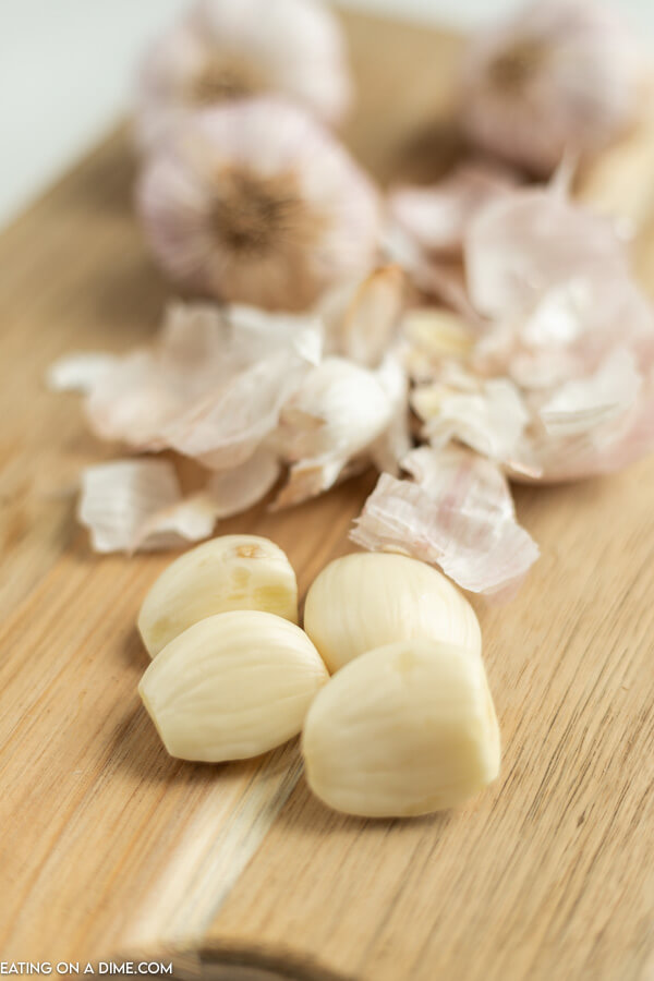 Close up image of slice garlic cloves on a cutting board with garlic peelings. 