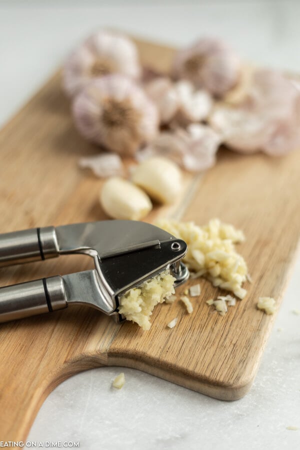 Close up image of garlic press and minced garlic with garlic cloves on a cutting board. 