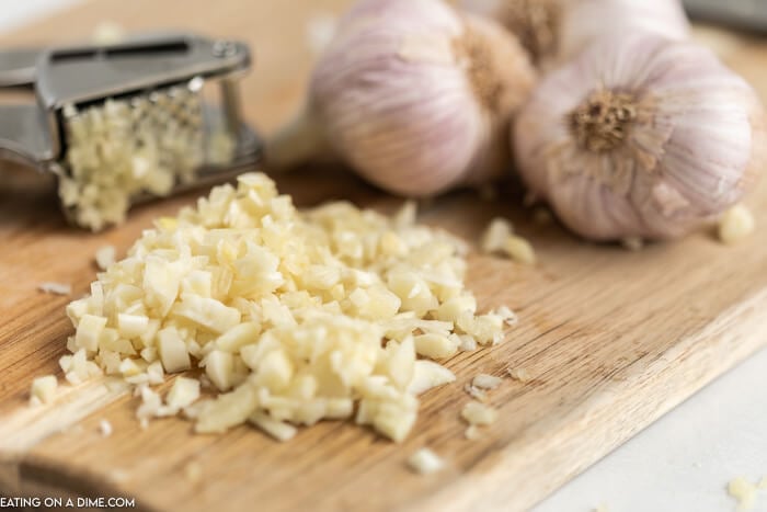 Close up image of chopped garlic cloves on a cutting board with a garlic press. 