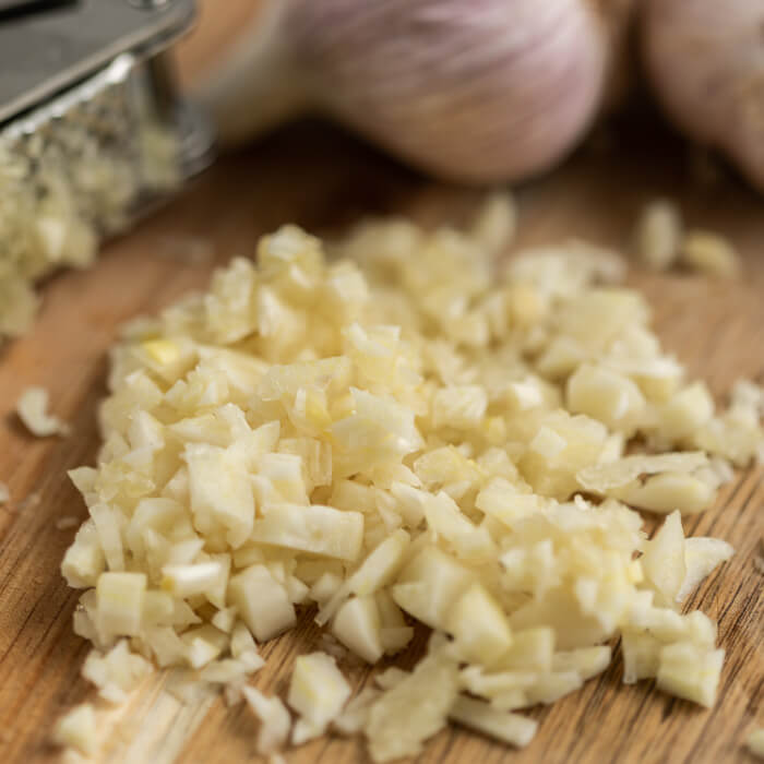 Close up image of chopped garlic cloves on a cutting board. 