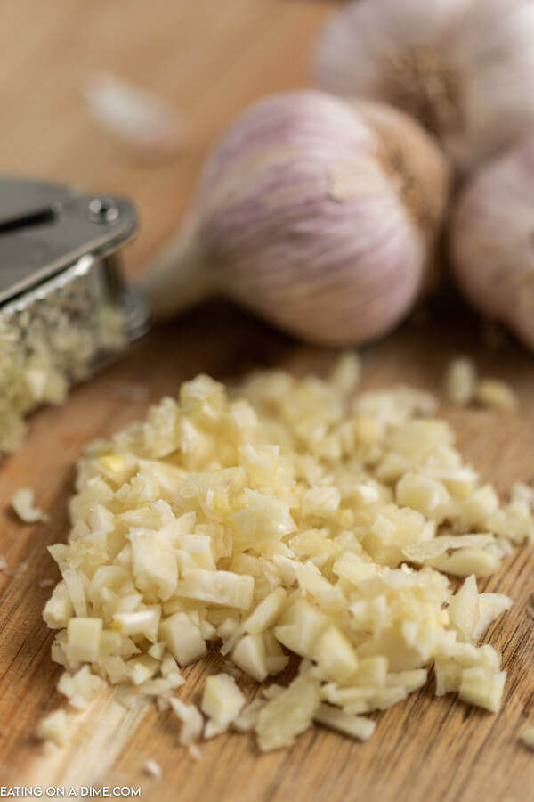 Close up image of minced garlic with a garlic press and garlic cloves. 