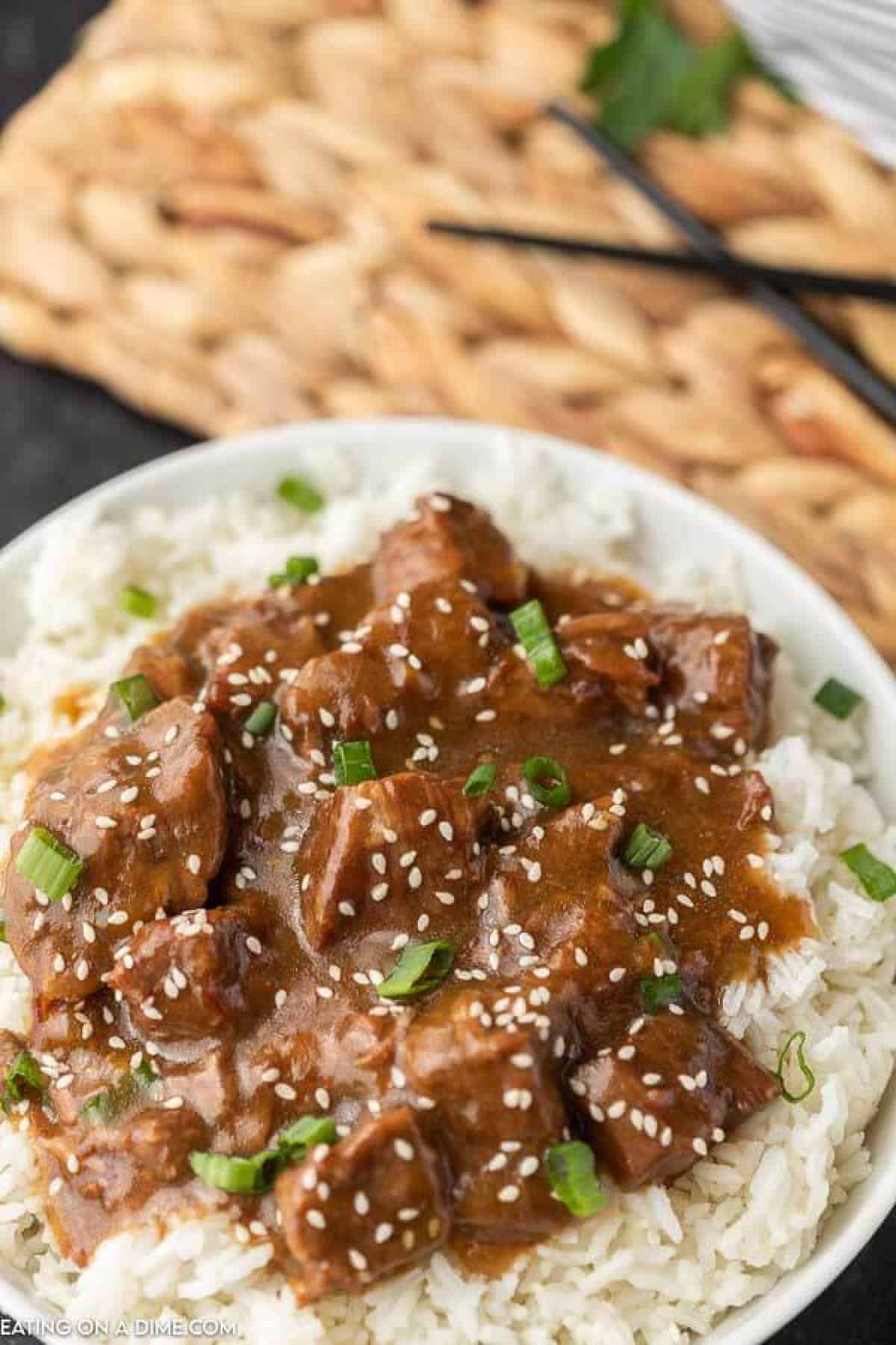 Instant Pot Teriyaki Beef over rice topped with green onions and sesame seeds with chop sticks in the back ground