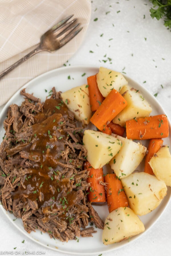 Plate with roast and gravy beside carrots and potatoes. 