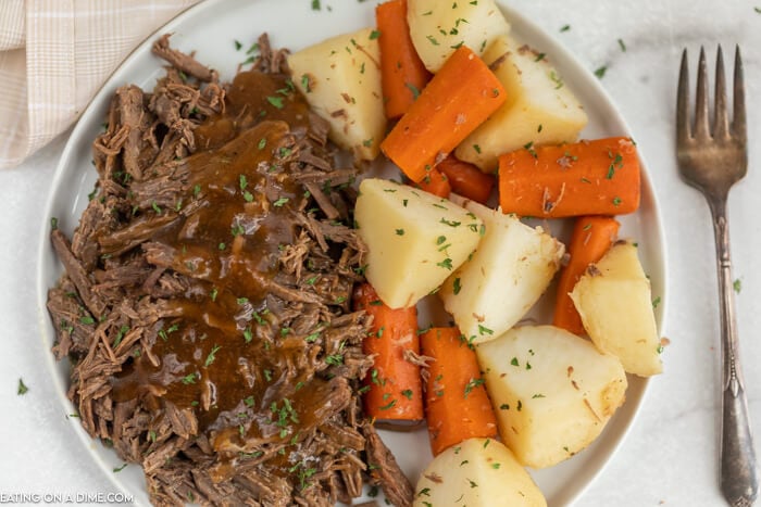 White plate with shredded roast topped with gravy beside carrots and potatoes. 