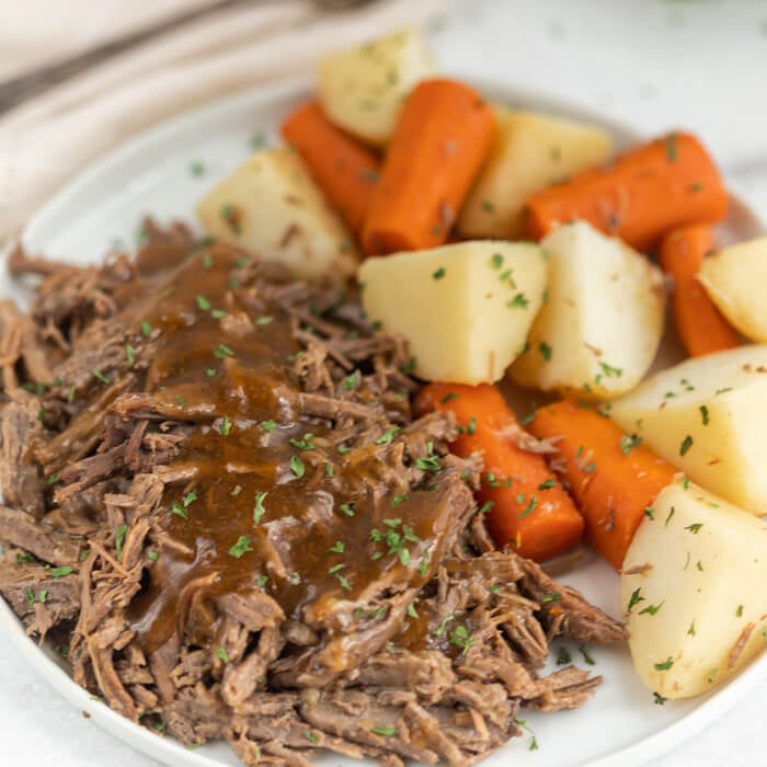 Plate with roast topped with gravy served with potatoes and carrots. 