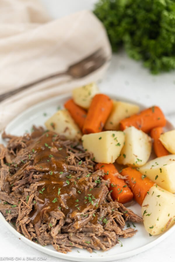 Plate with roast topped with gravy beside carrots and potatoes. 