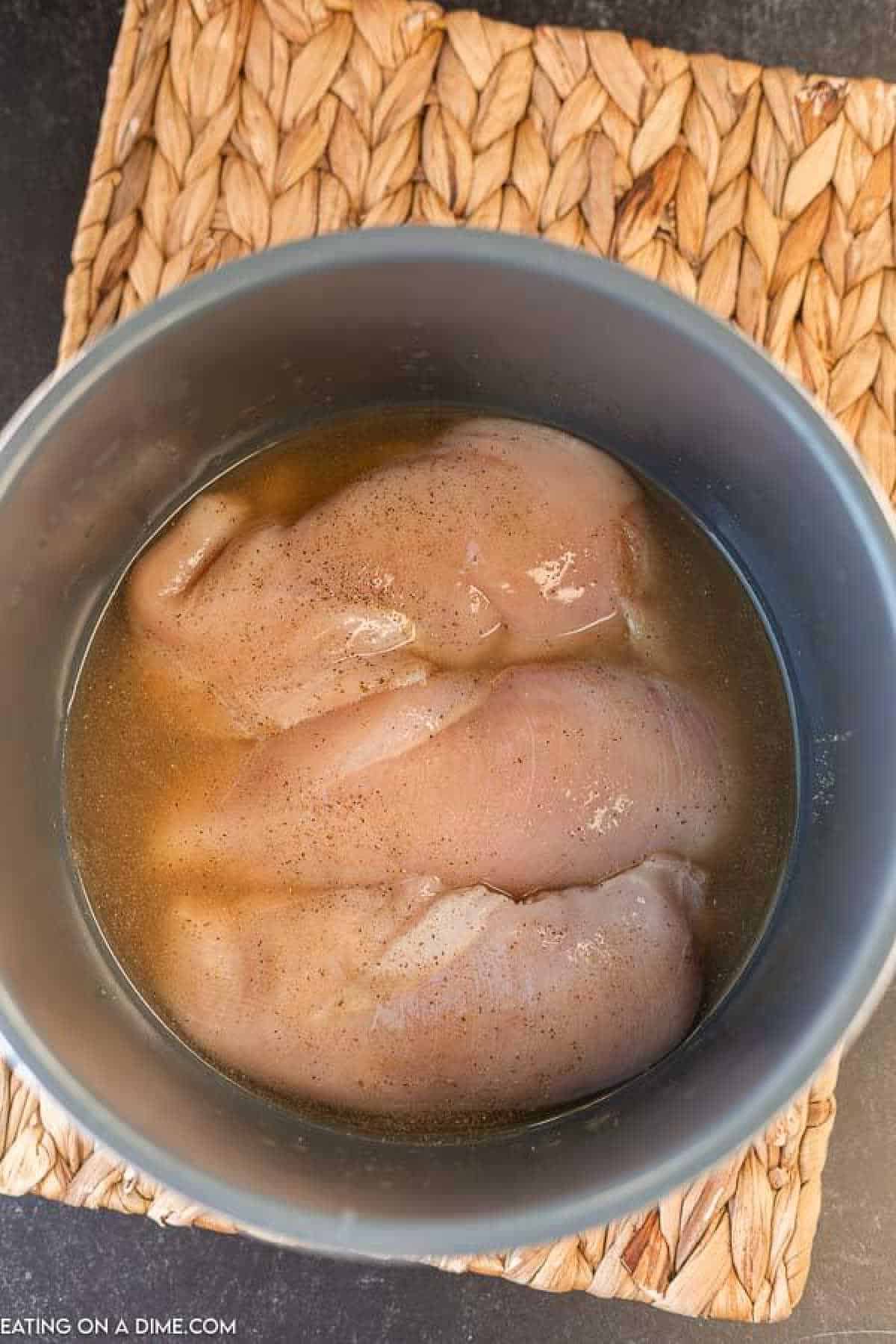 Raw chicken breast in the instant pot seasoned and chicken broth added.
