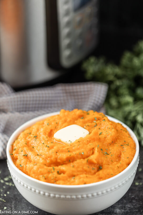 Bowl of mashed sweet potatoes topped with butter. 
