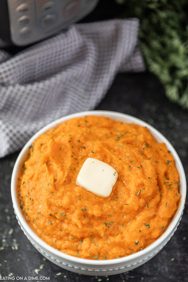 Bowl of mashed sweet potatoes topped with butter. 