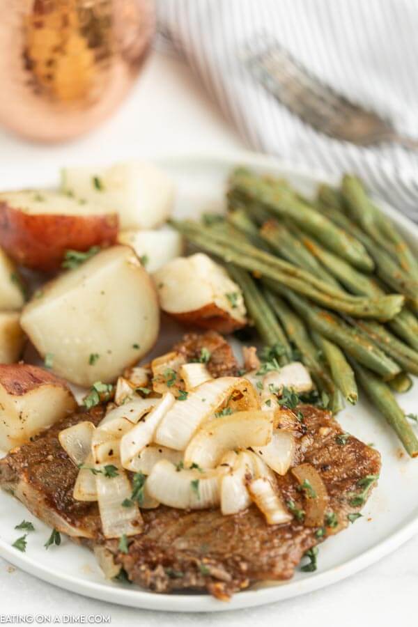 Close up image of steak and onions and potatoes and green beans on a white plate. 