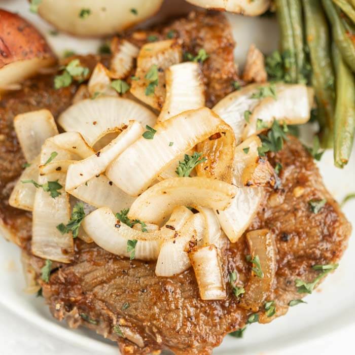 Close up image of steak with onions and potatoes and green beans. 