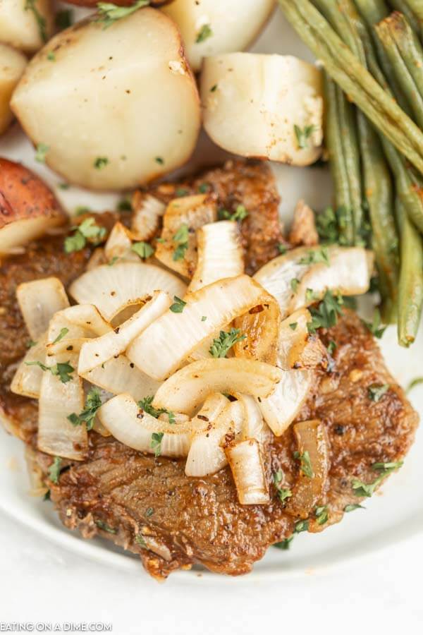 Close up image of steak with onions on top and potatoes and green beans. 