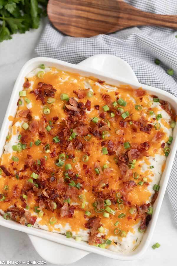 Overview of the loaded mashed potatoes in a white casserole dish topped with cheese, bacon and chives. 
