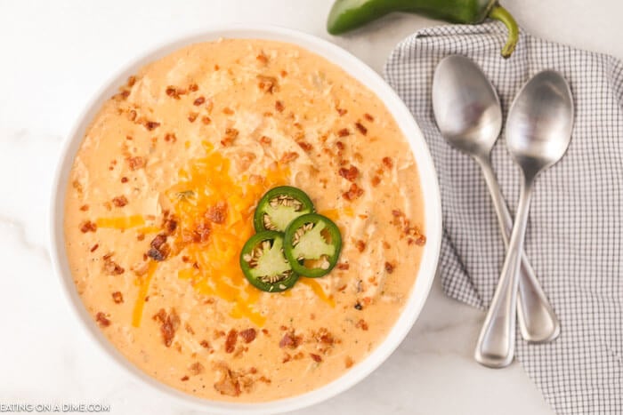 Close up image of a white bowl of Jalapeno Popper Chicken Soup with two spoons and a jalapeno. 
