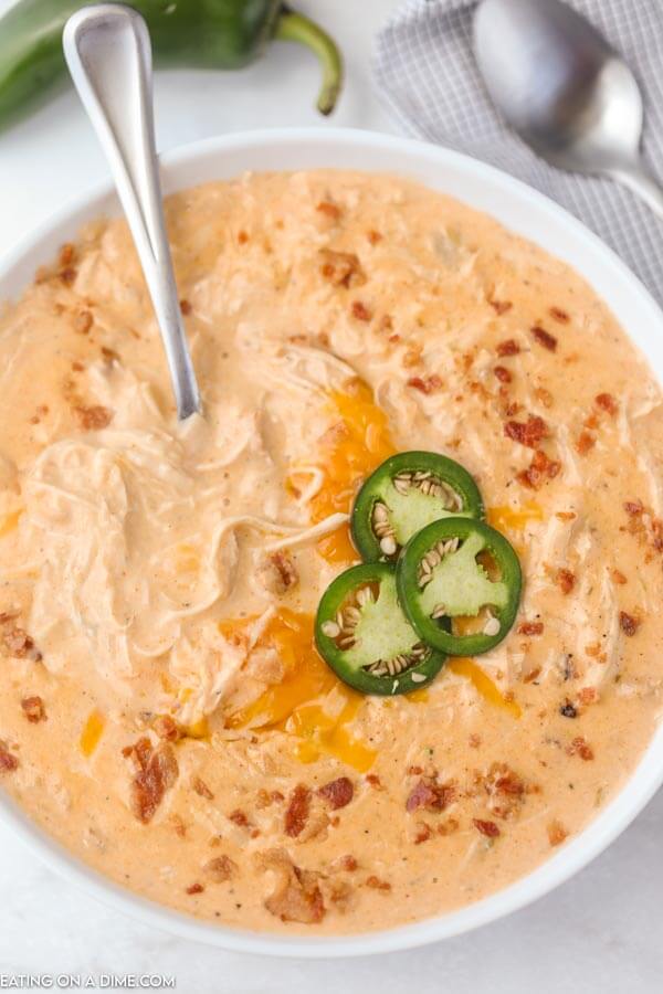 Close up image of a white bowl of Jalapeno Popper Chicken Soup with a spoon in the soup. 