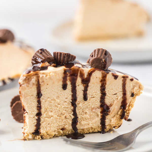 Close up image of a slice of peanut butter pie topped with mini peanut butter cups on a plate with a fork. 