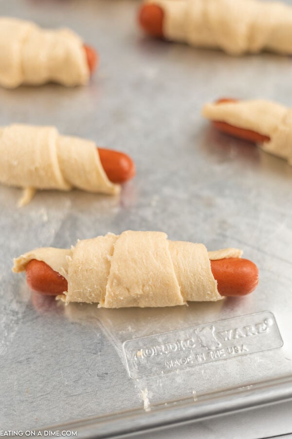 Uncooked pigs in a blanket on a baking sheet. 