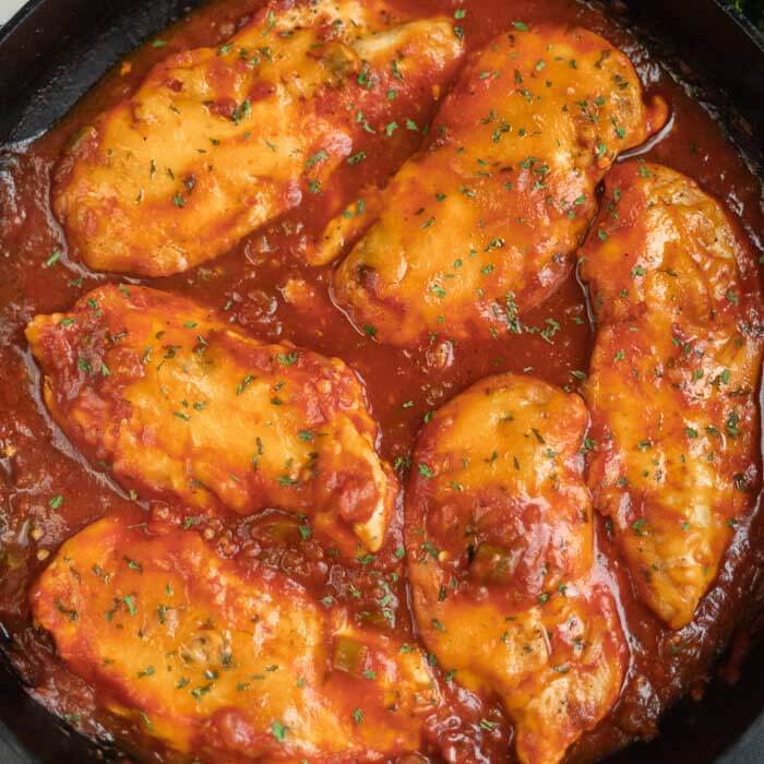 Close up of 6 chicken breasts in a cast iron skillet topped with salsa and cheddar cheese 