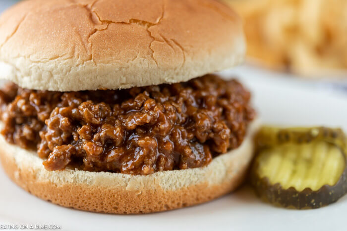 Close up image of sloppy joes on a buns with pickles on the side. 